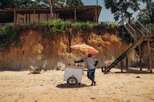 A beach vendor with an ice cream cart under an umbrella at Nazaré Beach, Brazil.